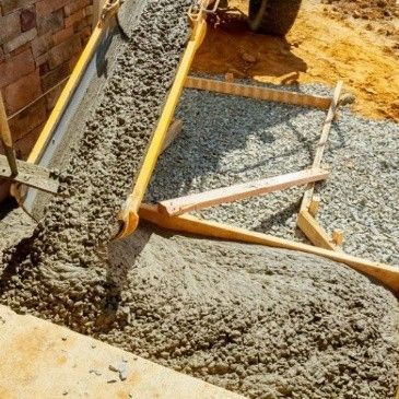 wet concrete being poured from a chute into a wooden frame filled with gravel at a construction site. wet concrete being poured from a chute into a wooden frame filled with gravel at a construction site.
