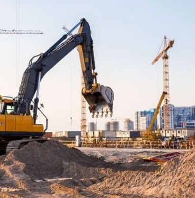 Photograph of a construction site featuring a yellow excavator with its bucket raised above a large pile of dirt. Photograph of a construction site featuring a yellow excavator with its bucket raised above a large pile of dirt.