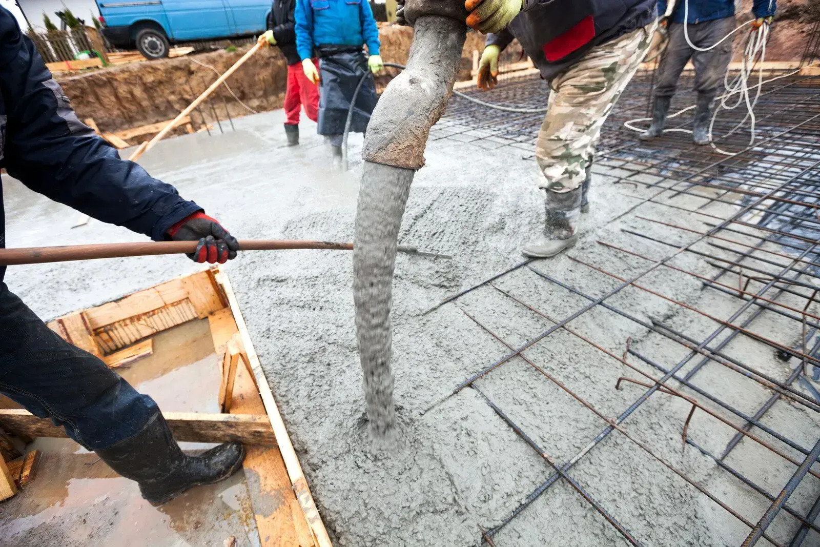 construction workers pouring wet concrete over a steel rebar grid for foundation reinforcement.
