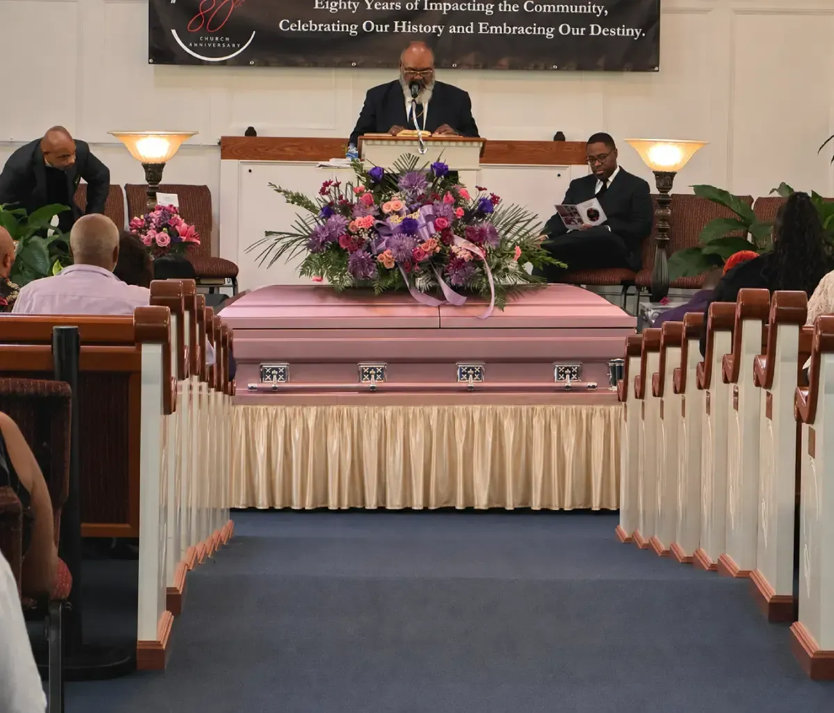 Church service with a speaker at the pulpit and floral arrangement on the stage, viewed from the aisle