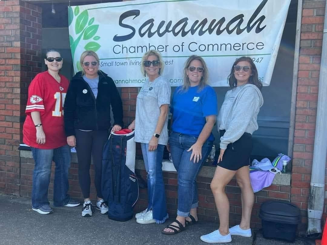 Five people pose in front of a Savannah Chamber of Commerce banner, brick building.