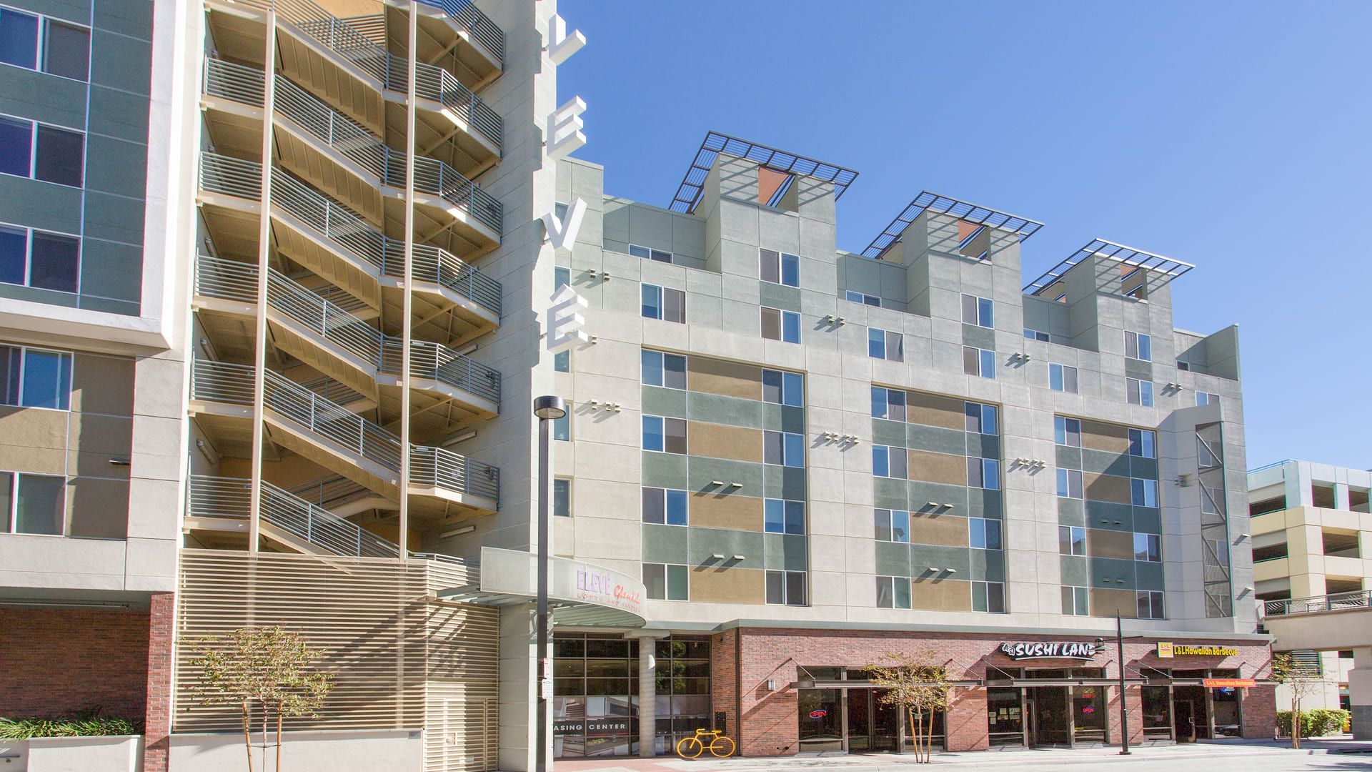Multi-story apartment buildings, one with external stairs, over retail stores on a sunny day.