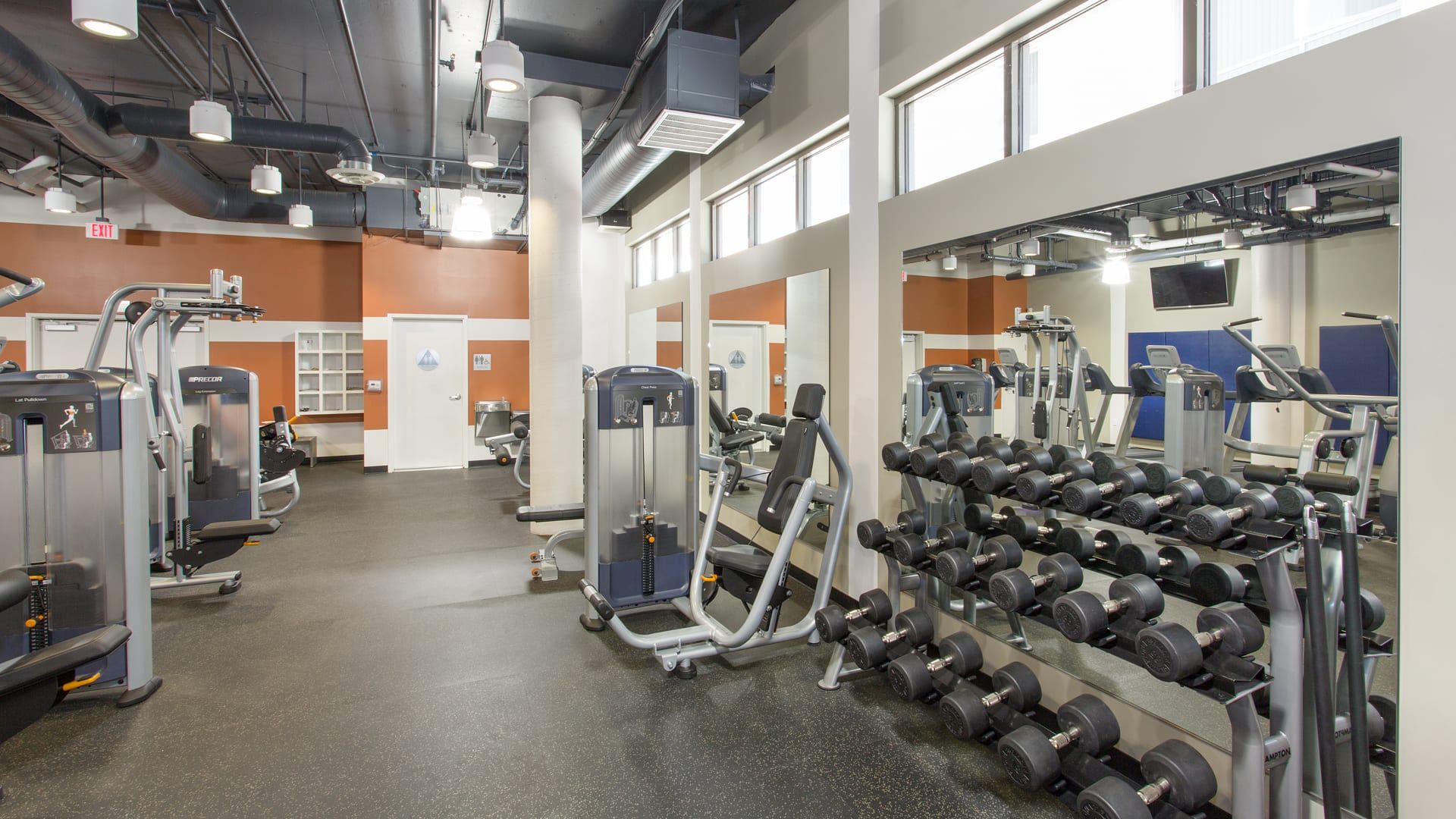 Gym interior with weight machines, dumbbells, and large mirrors on the wall.