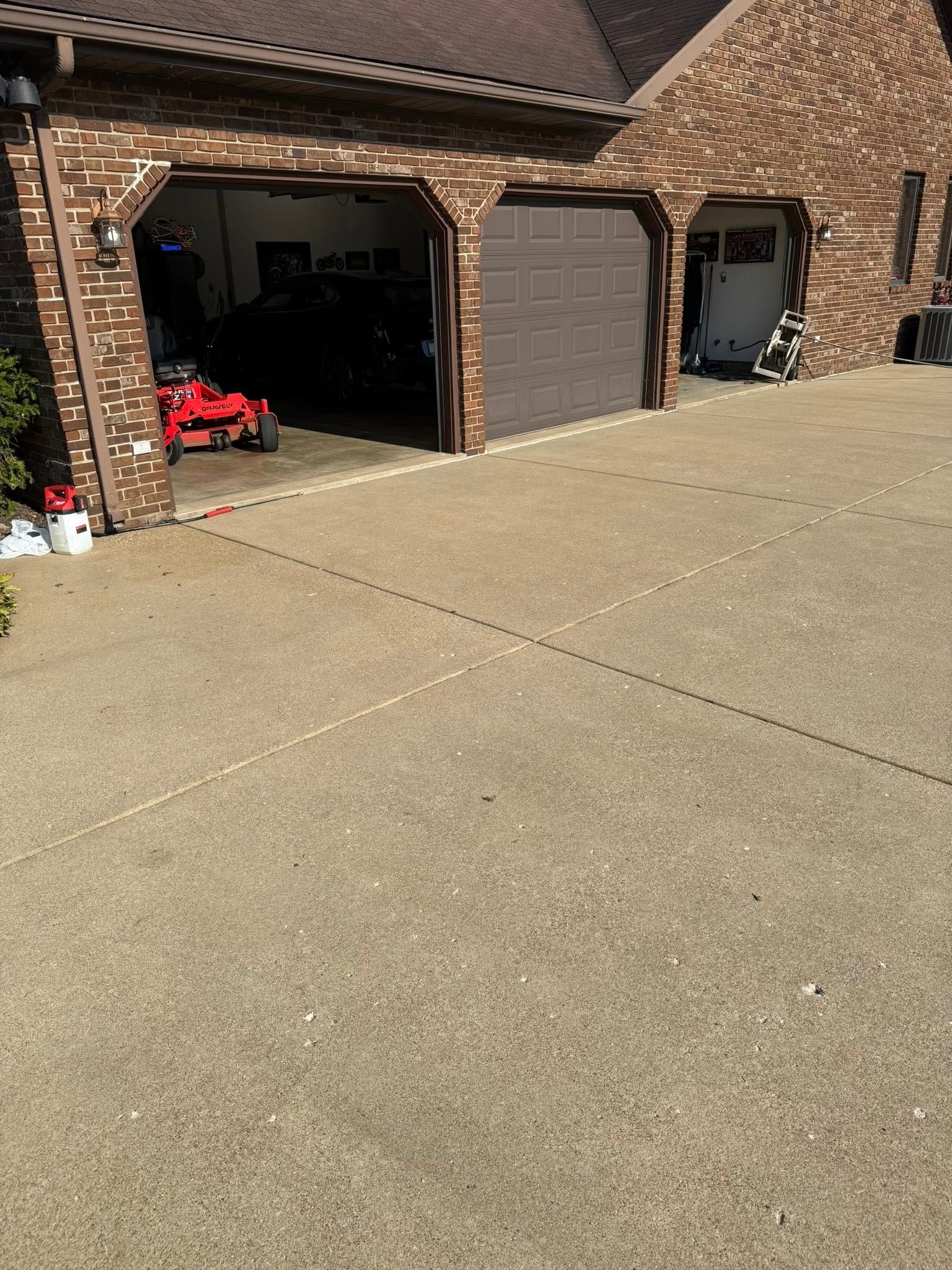 Driveway leading to a three-bay garage with brick exterior, one open bay with red mower.