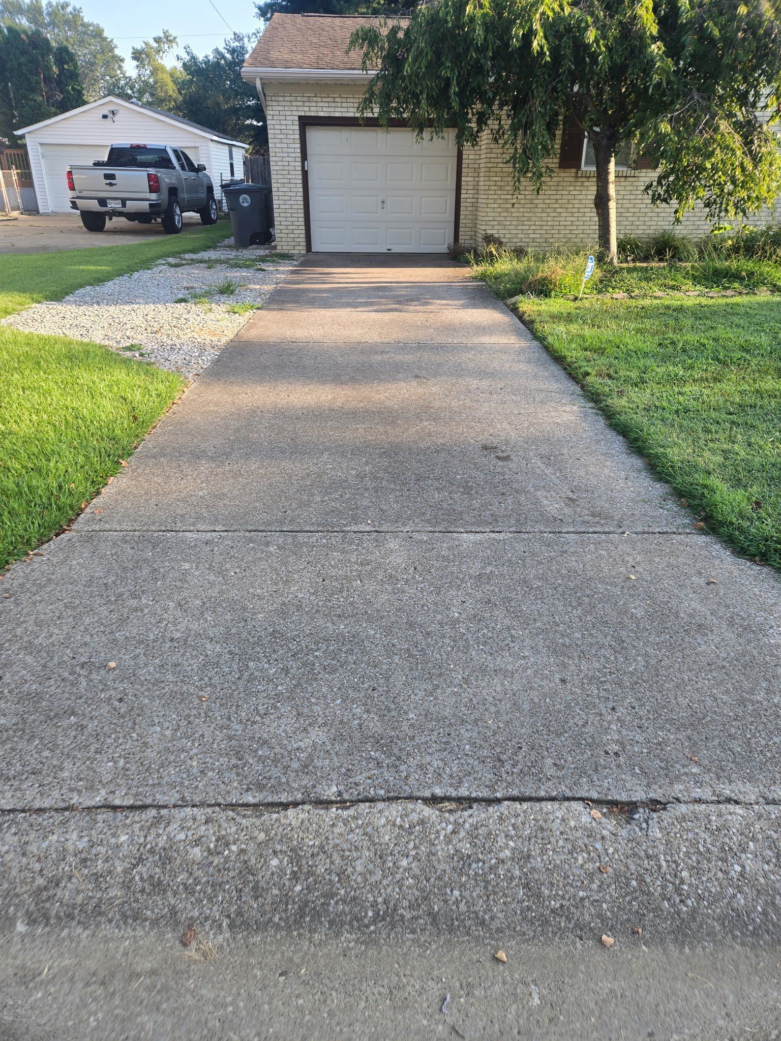 Concrete driveway leading to a garage with a truck parked in the background. Green grass borders the driveway.