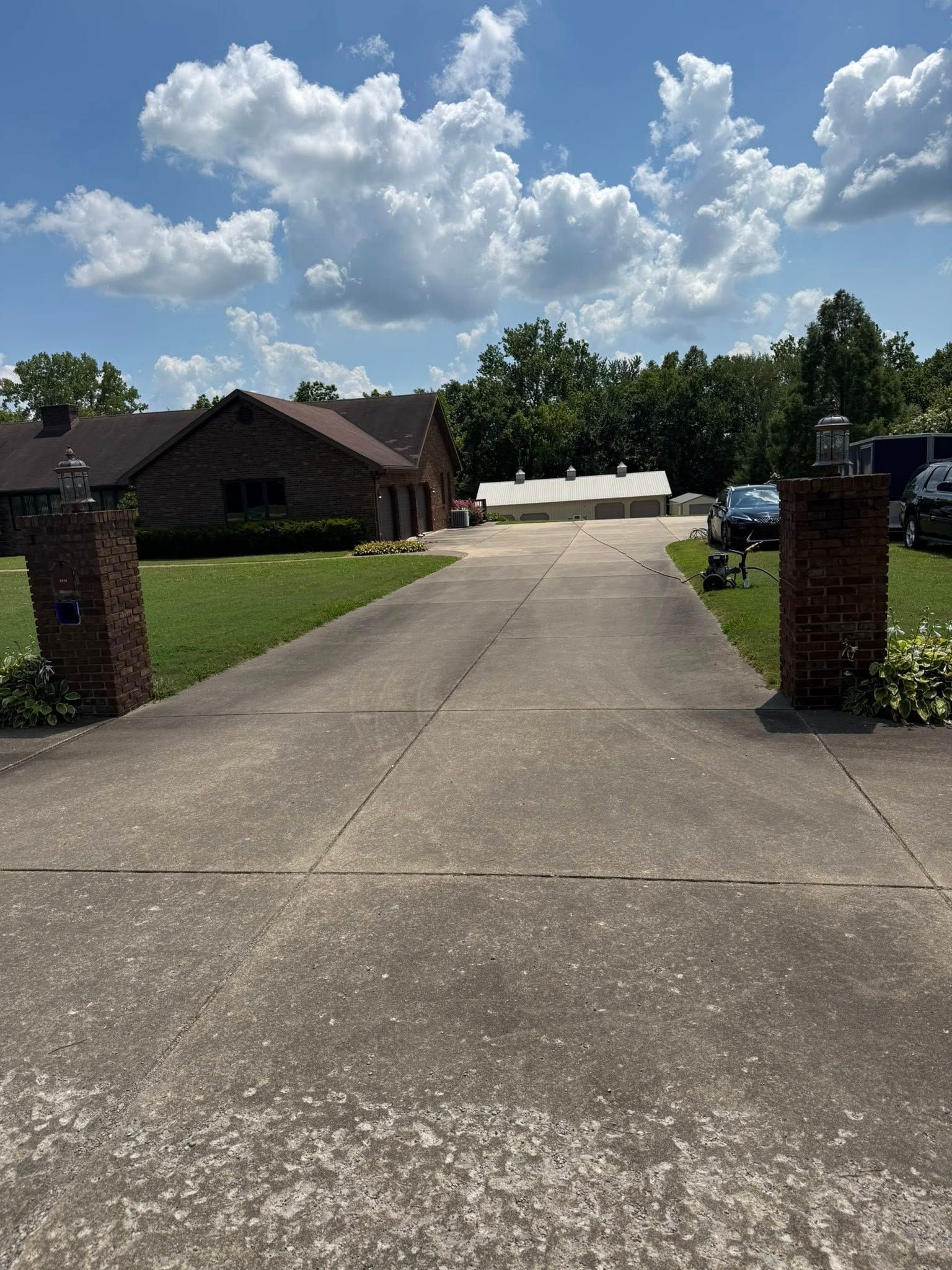 Driveway leading to a brick house under a blue sky with clouds. Two brick columns flank the entrance.