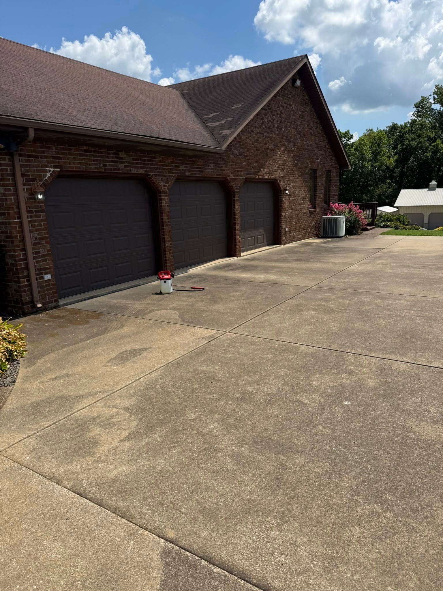 Brick garage with three dark brown garage doors, concrete driveway, and blue sky.
