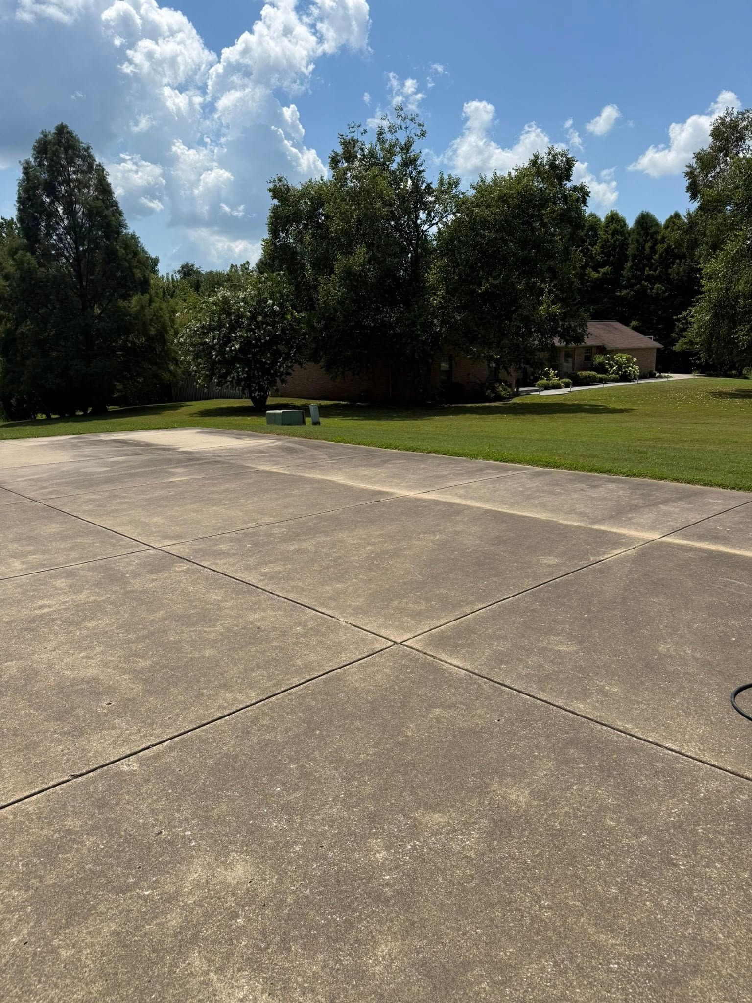 Concrete patio with trees and a house in the background under a blue sky with clouds.