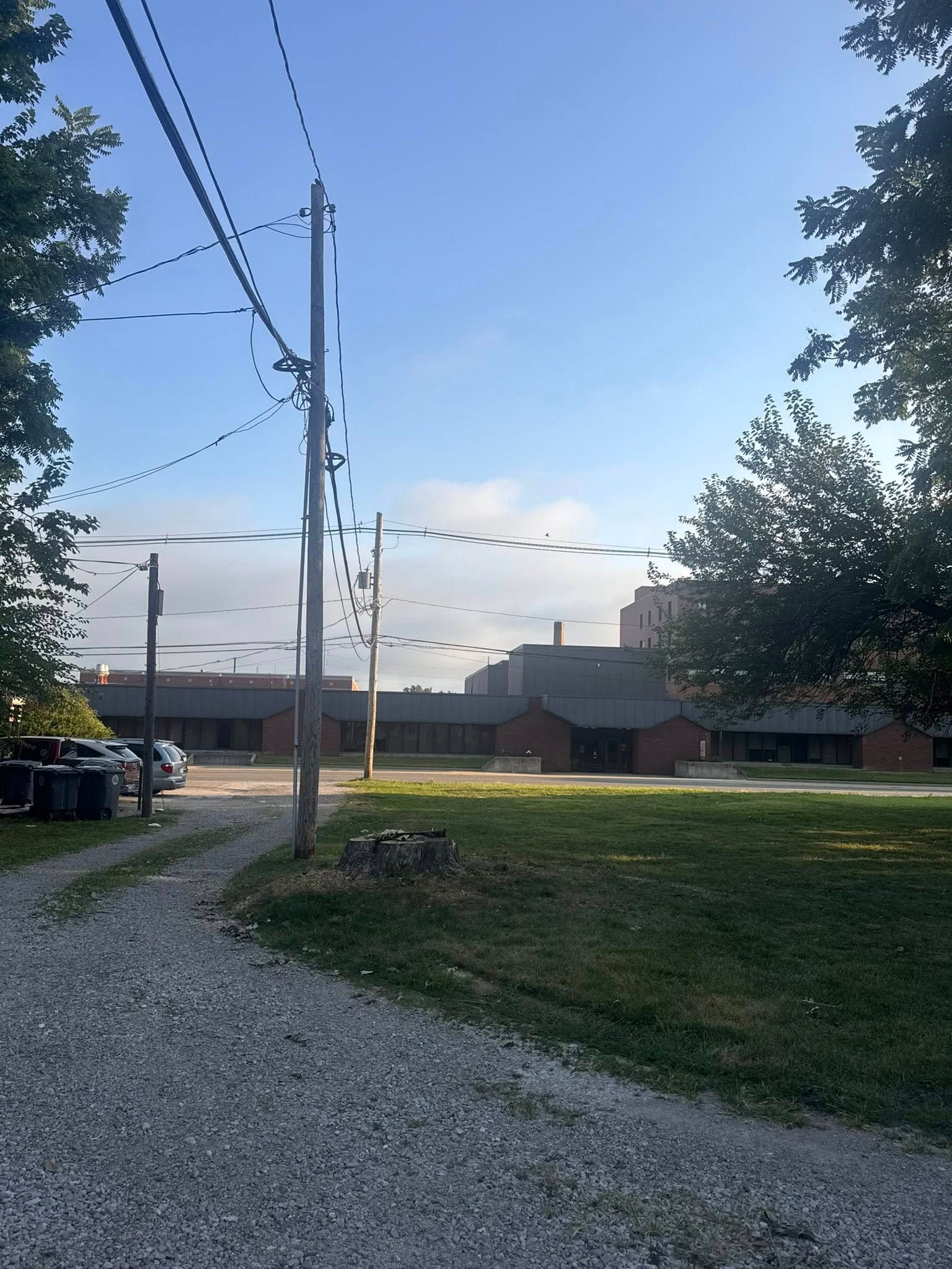 Gravel drive leads to a brick building under a clear blue sky, with power lines and trees.