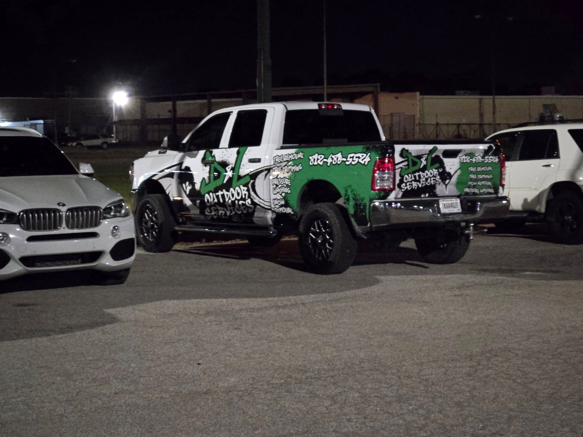 White Ram truck with green graphics parked next to white SUV and a BMW at night.