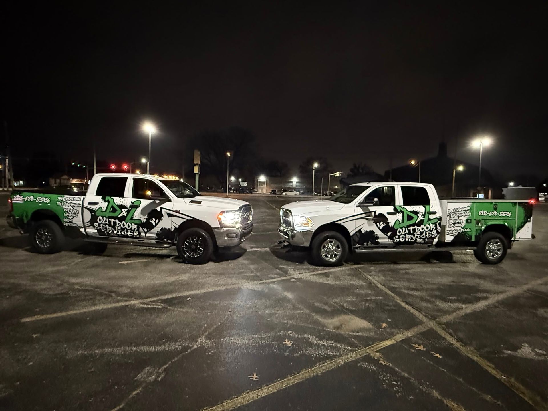Two white pickup trucks, branded with green and black logos, parked outdoors at night.