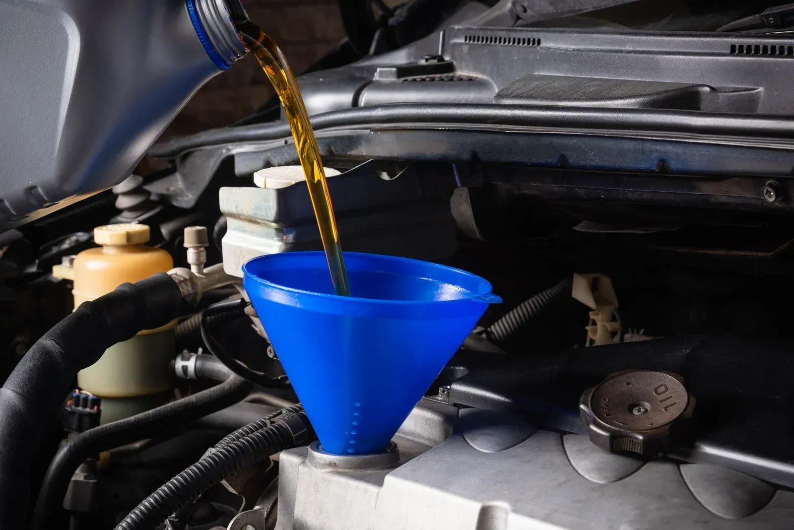 A blue funnel is being used to pour oil into a car engine.