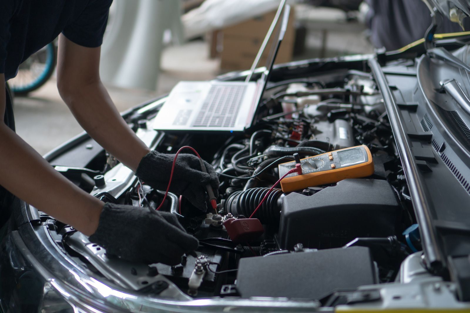 A man is working on the engine of a car with a laptop.