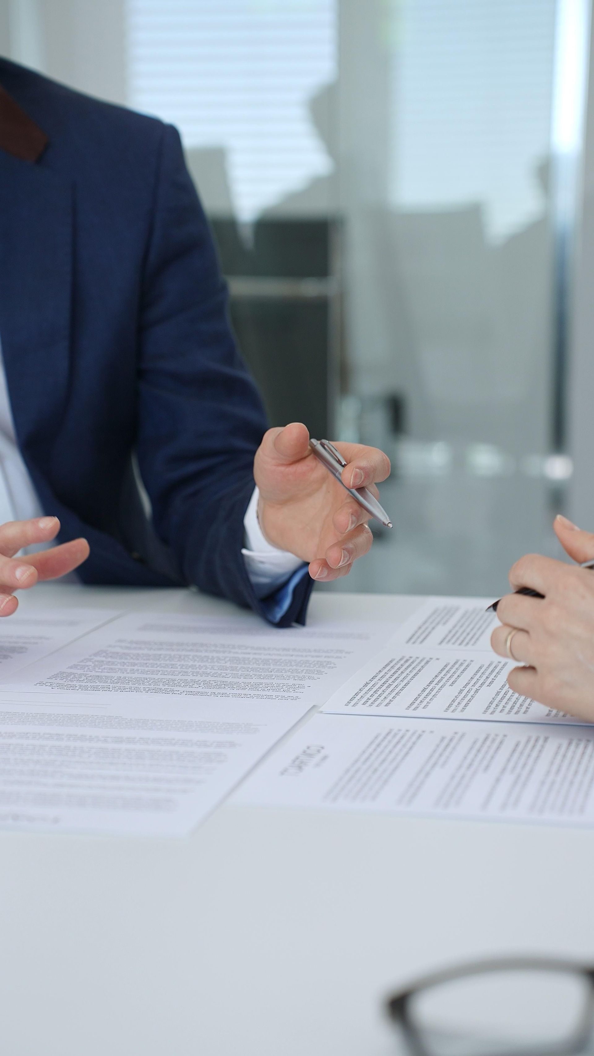 Two people in business attire reviewing documents and discussing a contract at a table