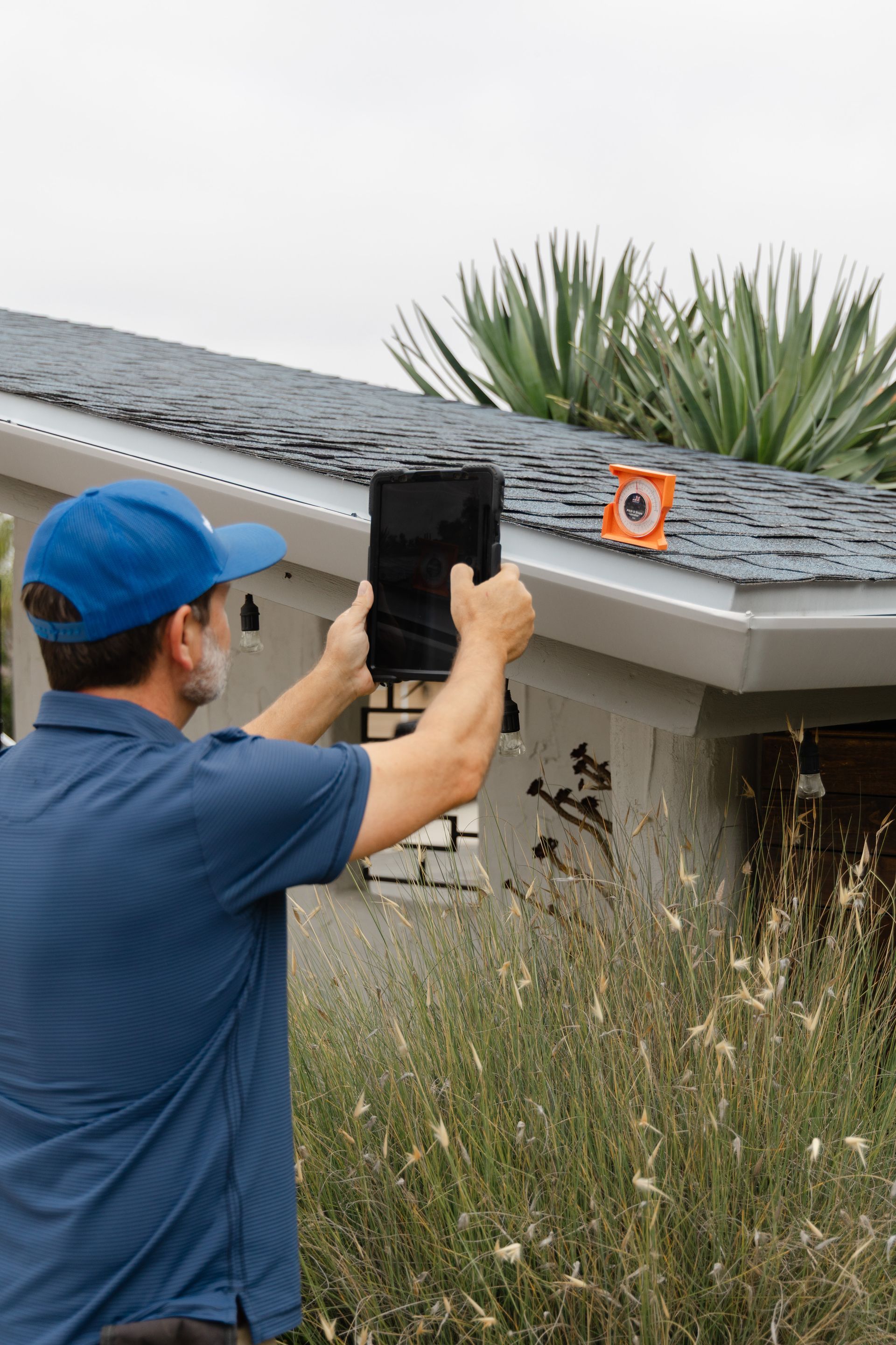 Person in blue cap using a tablet to inspect a rooftop with a small orange level marker