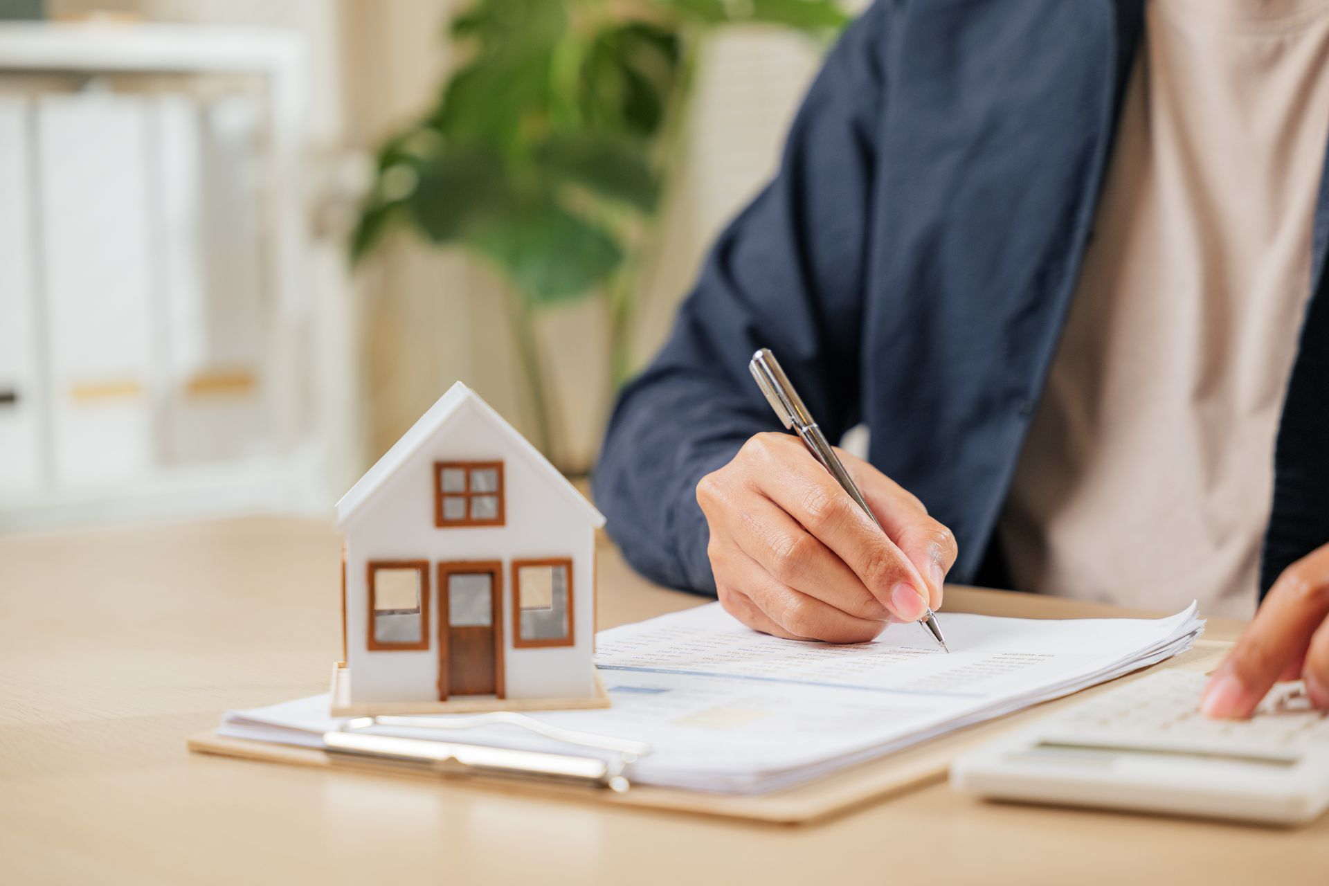 Hand writing on a notepad beside a small house model on a desk