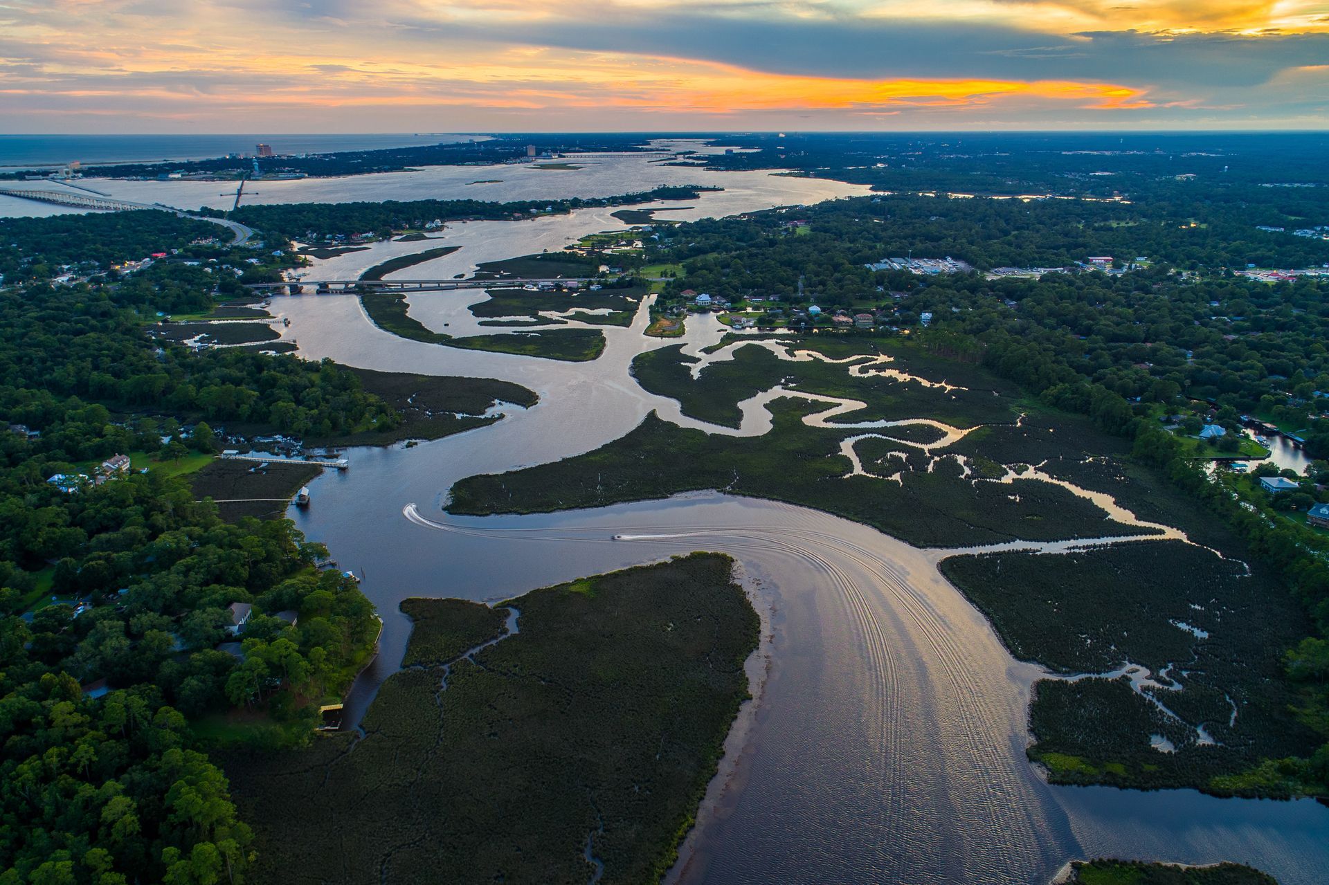 Aerial view of a winding river through lush green wetlands at sunset with a glowing orange sky