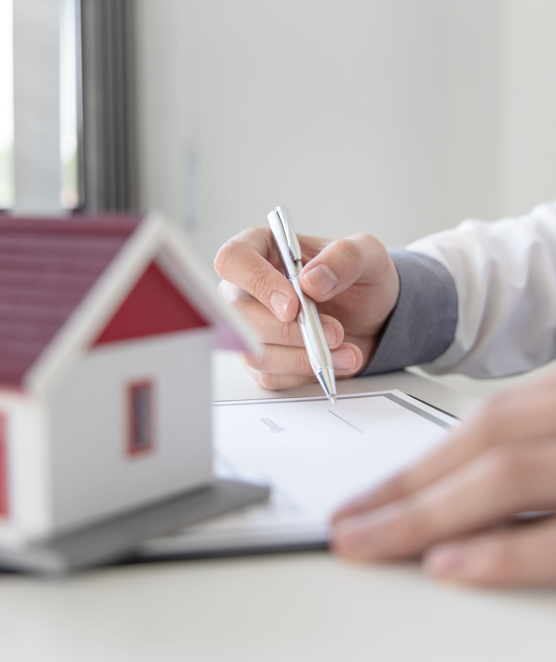 Hand drawing a house floor plan beside a small model house on a desk