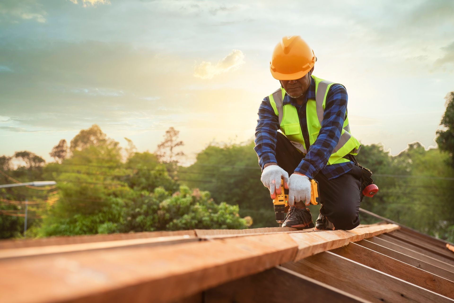 Construction worker in orange hard hat fastening roof planks with a power tool outdoors
