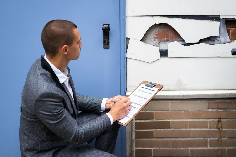 Man inspecting cracked drywall with clipboard beside a blue door