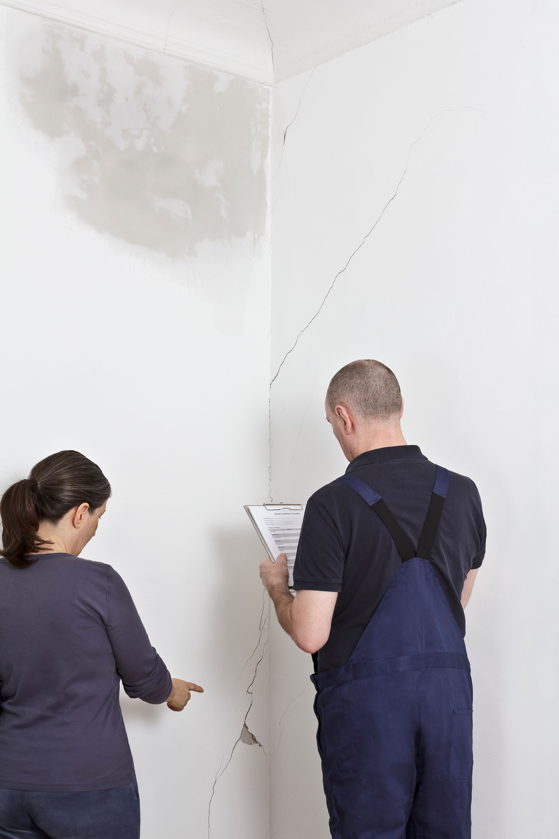 Two people examining a cracked wall with a clipboard in a bare room