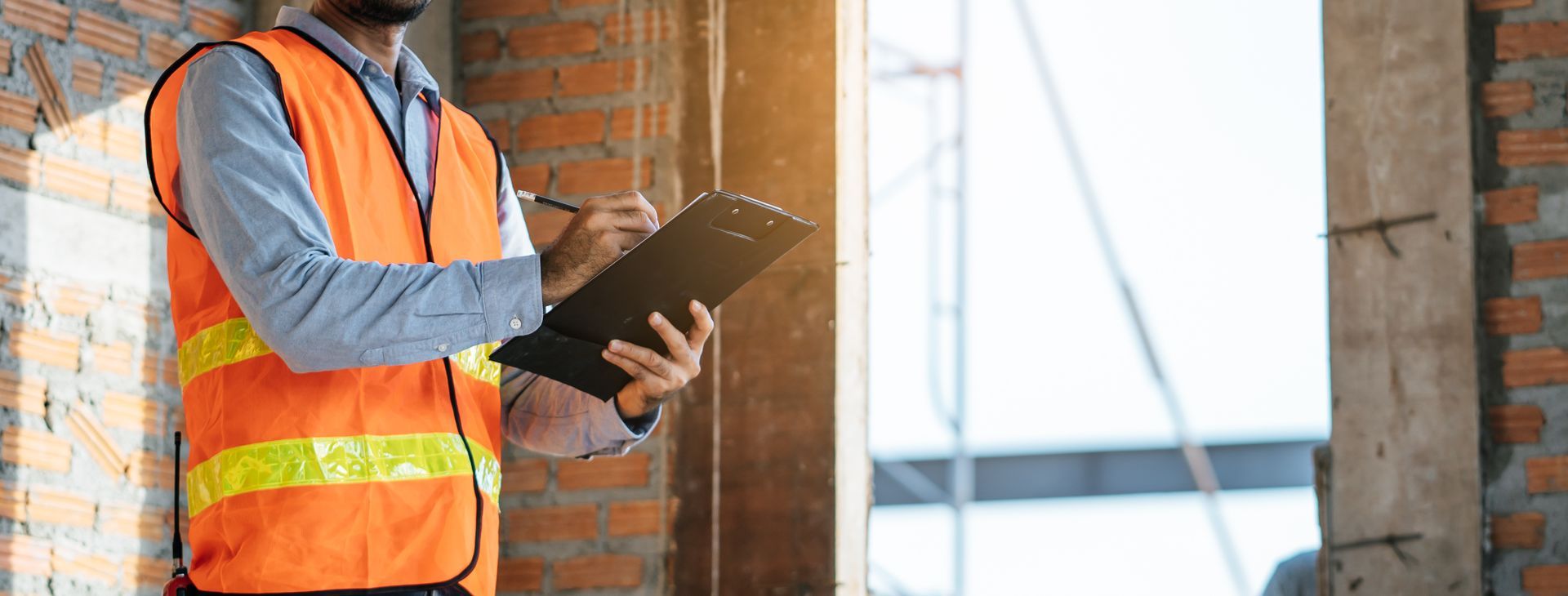 Construction worker in orange safety vest holding a clipboard at a building site