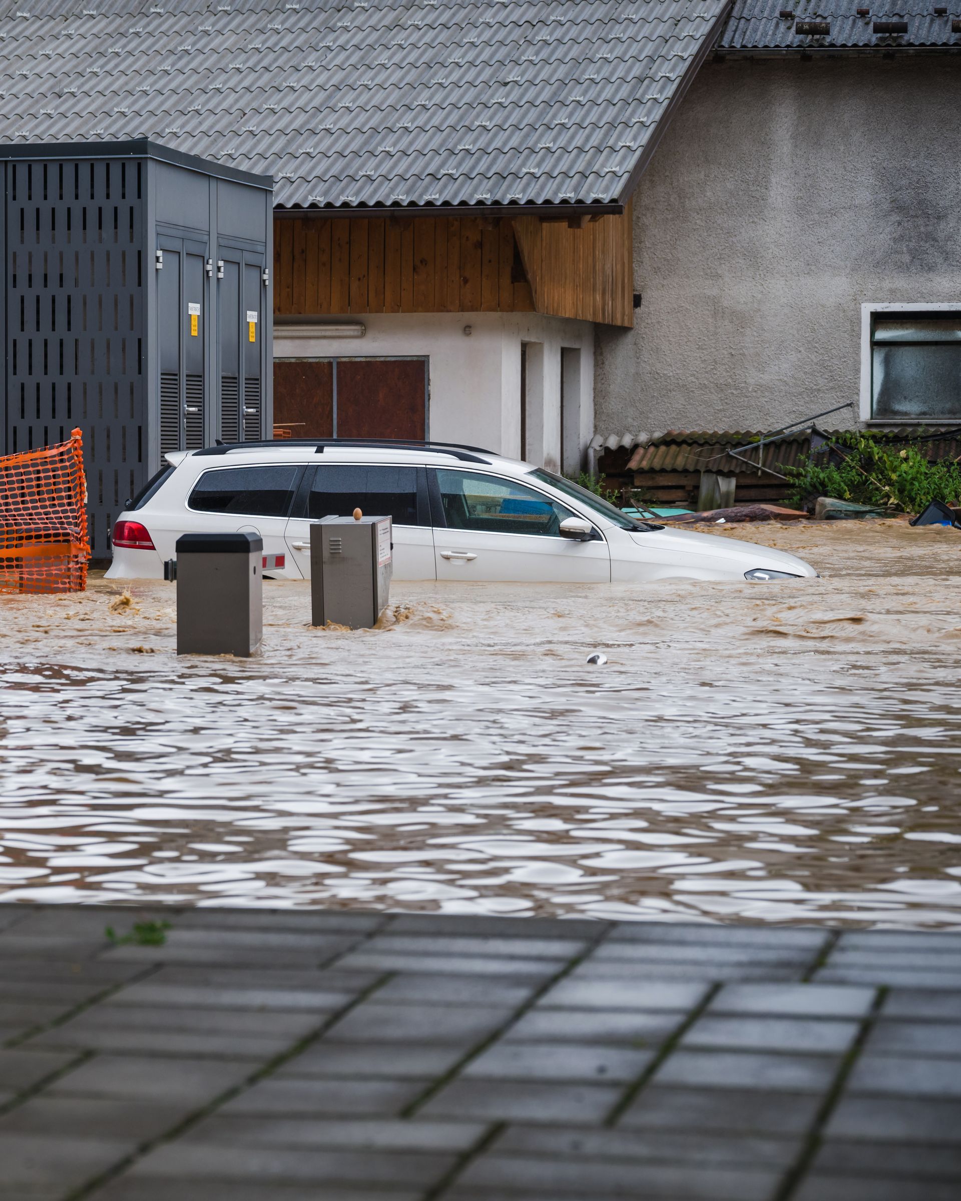 Flooded street with a partially submerged white car beside buildings and bins