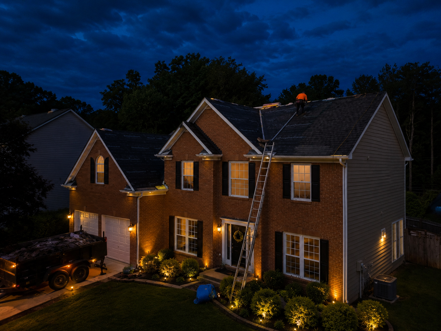 Two-story brick house at dusk with warm lights and lit windows under a dark blue sky