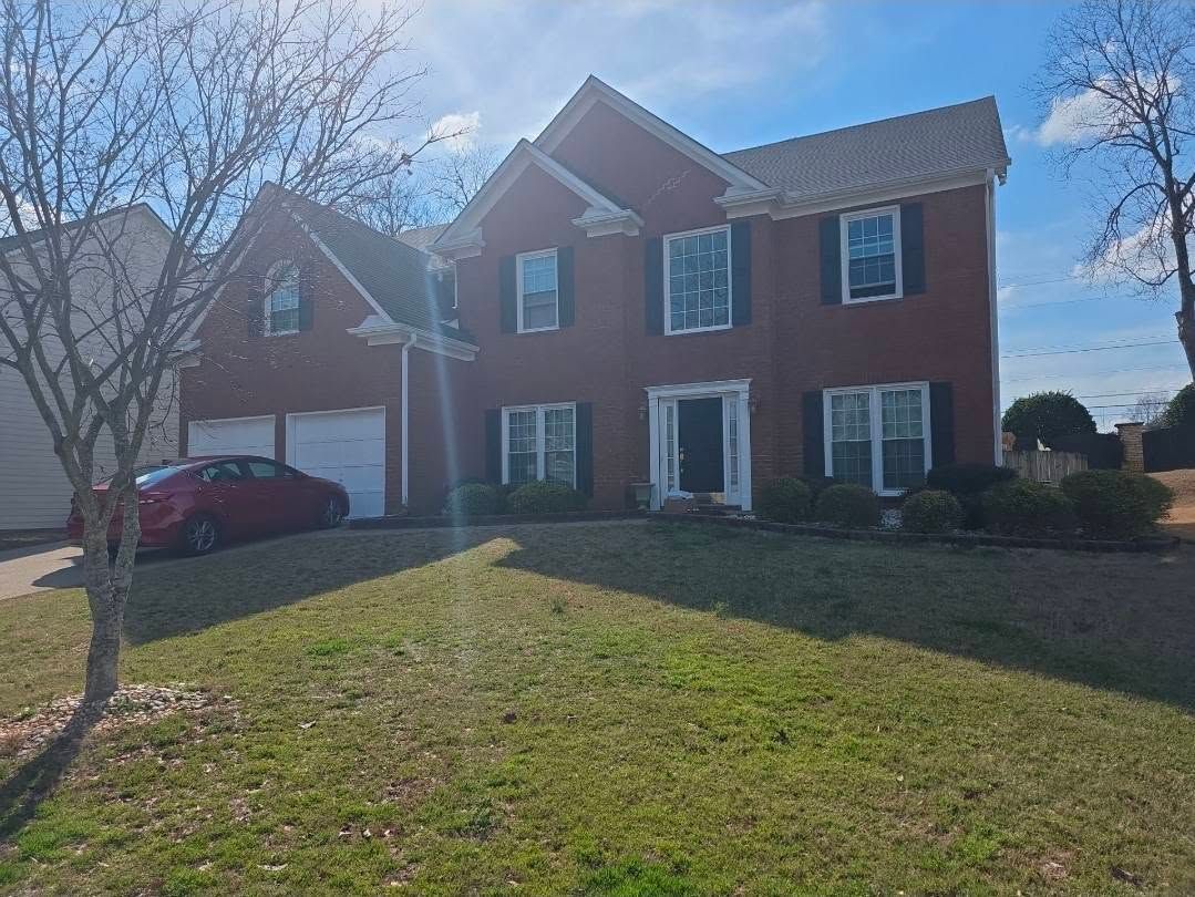 Two-story red brick house with white trim, a front lawn, and a red car parked on the left.