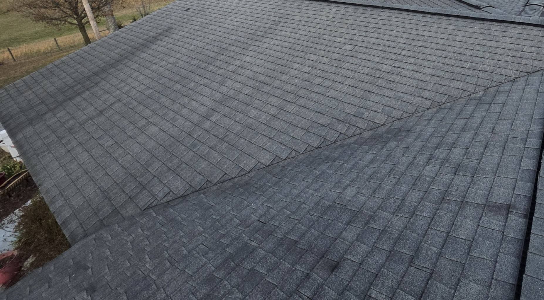 Gray shingle roof with intersecting slopes and a small puddle near the edge
