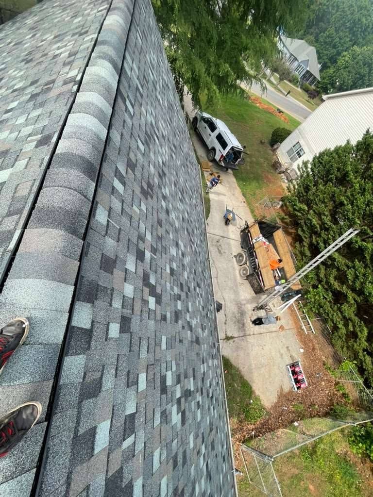 Roof edge overlooking a driveway with parked cars, trees, and people below in a residential yard