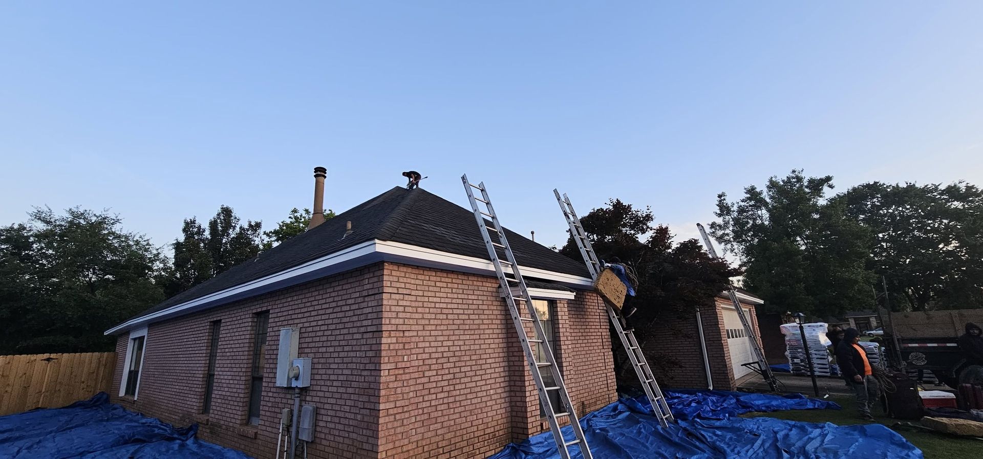 Damaged brick house with a collapsed roof and blue tarp covering debris in the yard