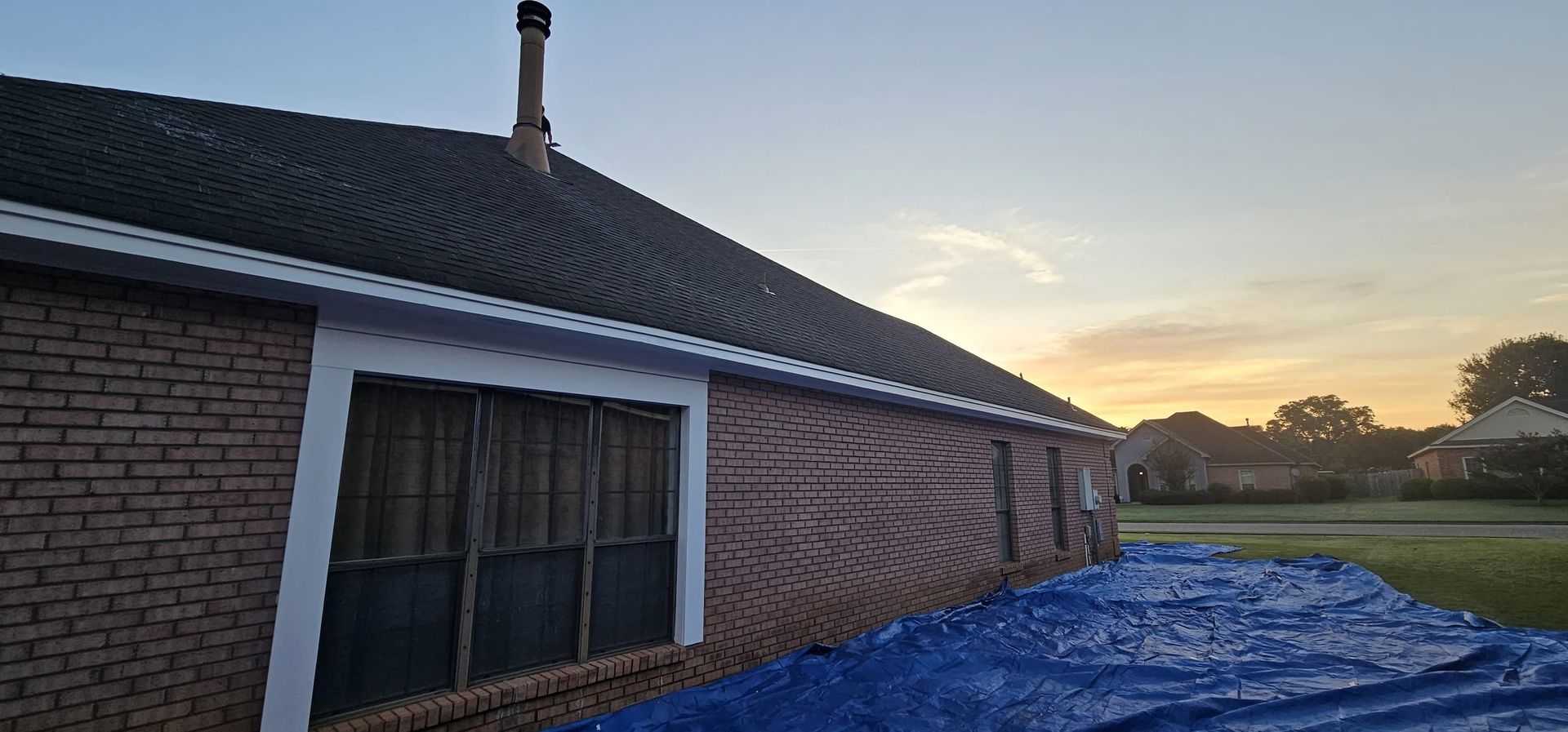 Brick house exterior at sunset with a blue tarp covering the ground by the wall