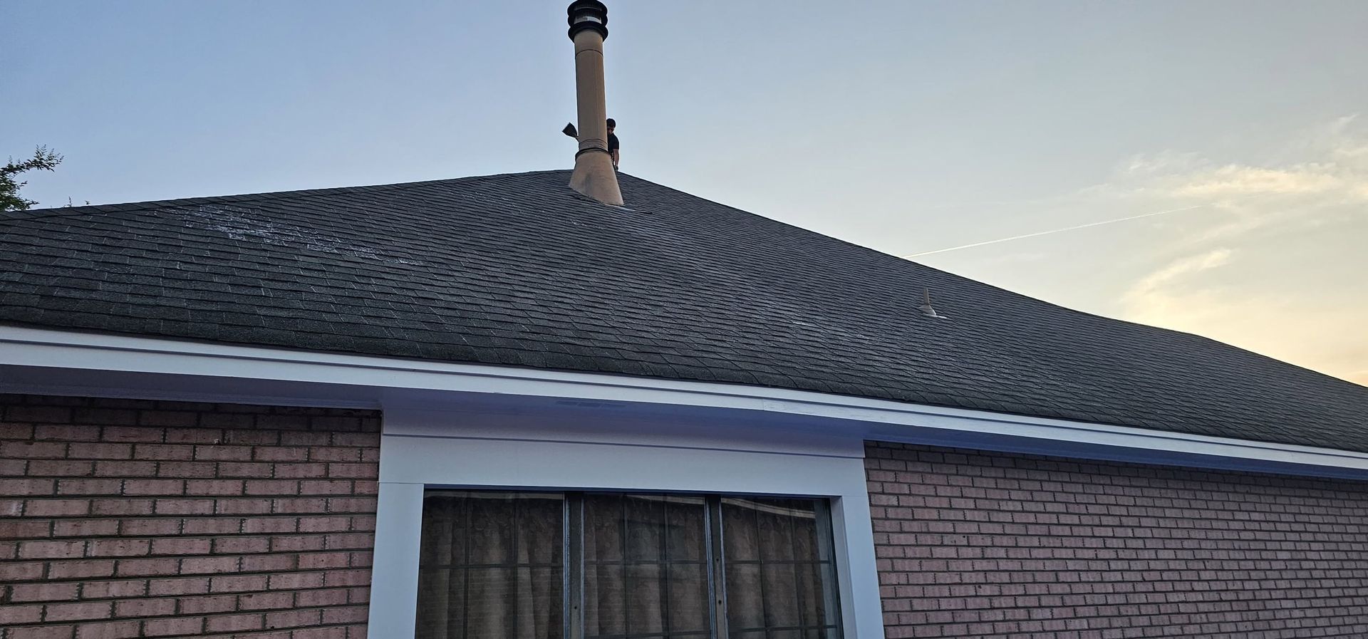 Brick house with a dark shingled roof and chimney at sunset