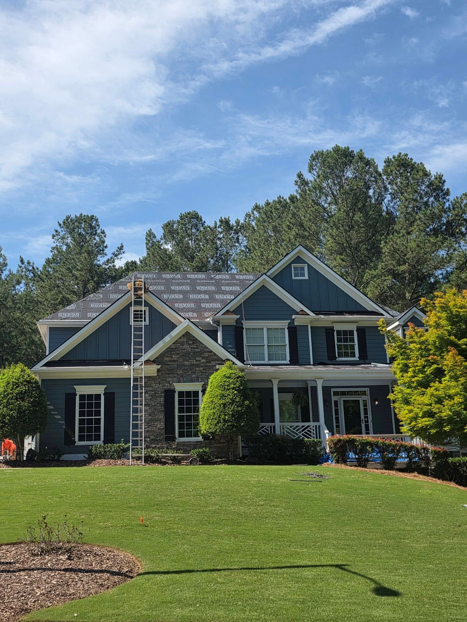 Blue house with white trim and a covered porch, set on a grassy lawn under a clear sky