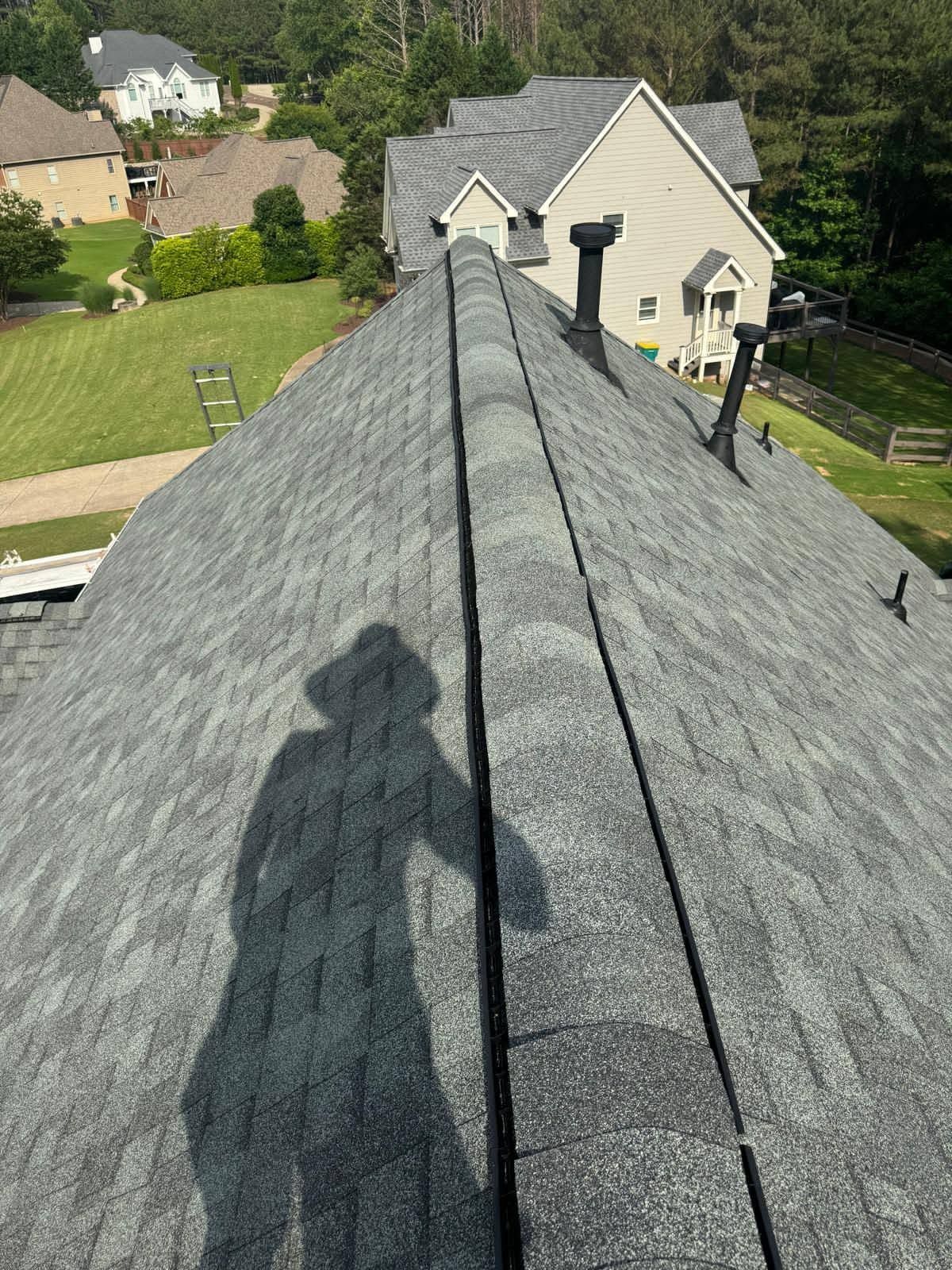 Roofer’s shadow on a gray shingle roof overlooking suburban houses and a green lawn