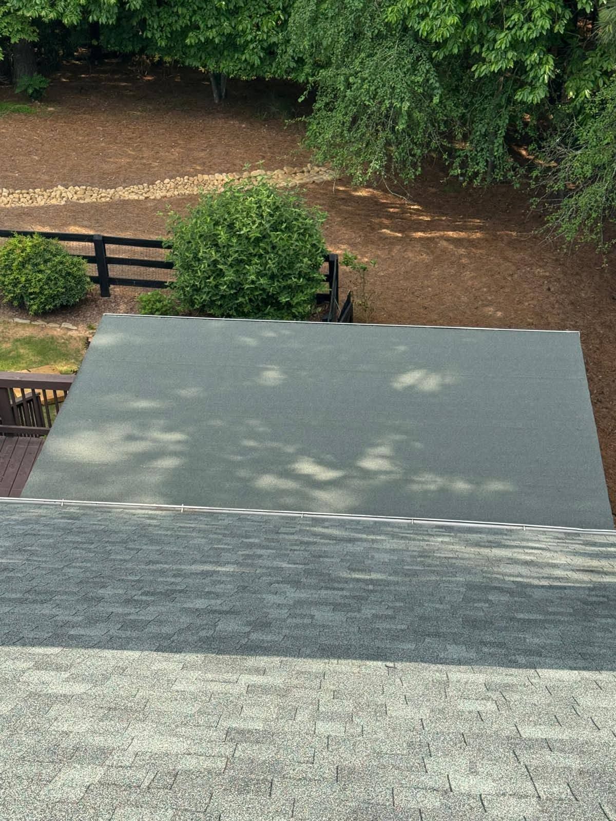 View from a roof down to a gray awning, dirt path, wooden gate, and green hedges in a garden