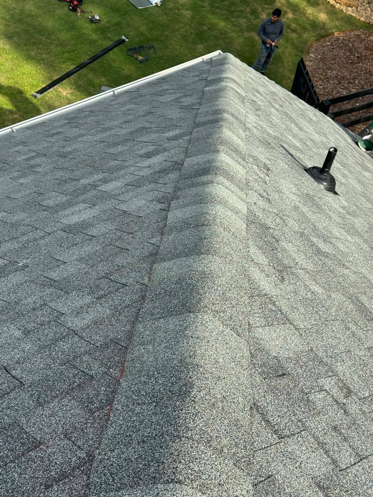 Steep gray shingled roof with a roof vent, viewed from above, with two people on the ground nearby