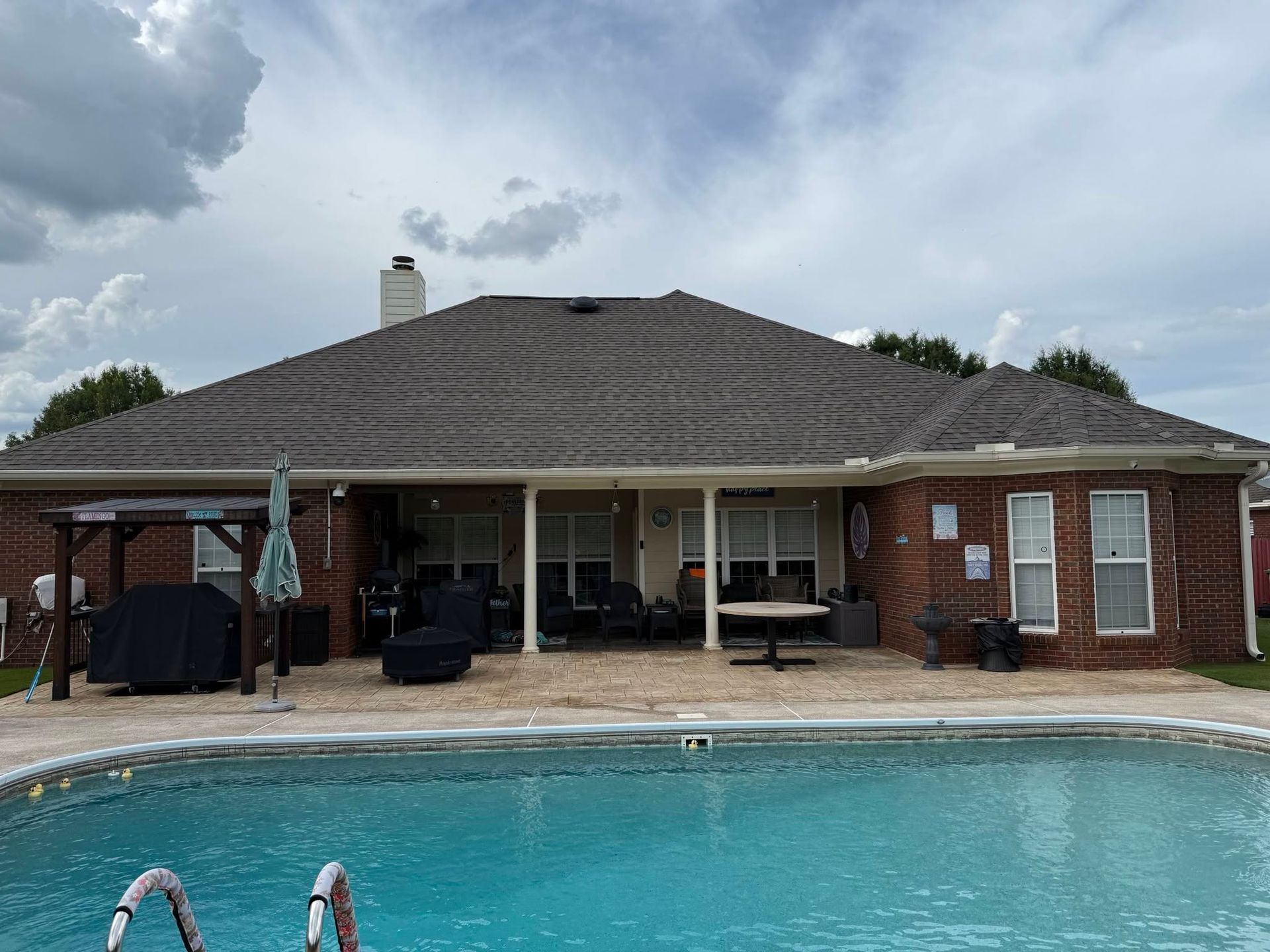 Backyard patio with a swimming pool and brick house under a cloudy sky