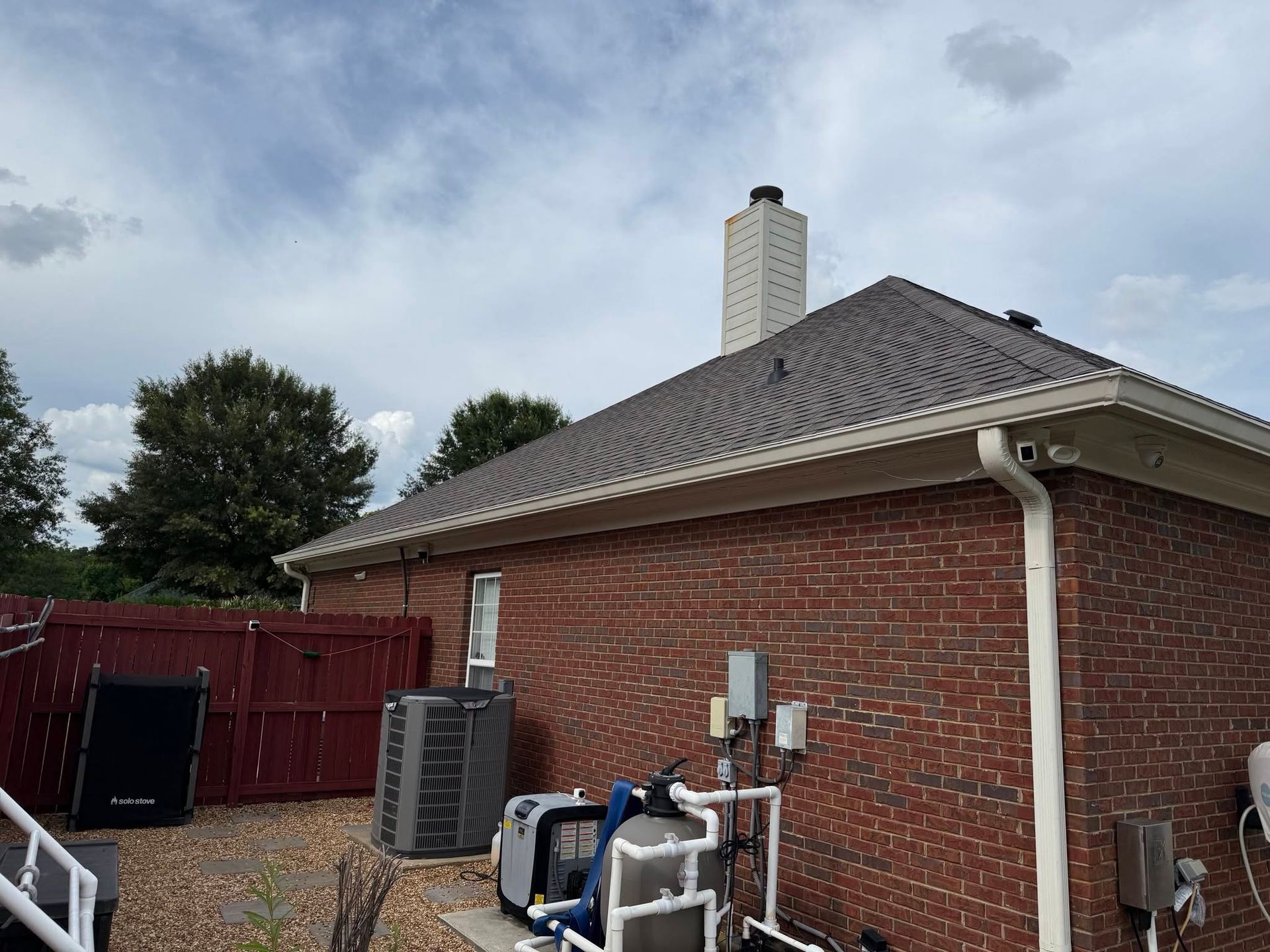 Backyard patio beside brick house with rooftop chimney, HVAC units, and red privacy fence