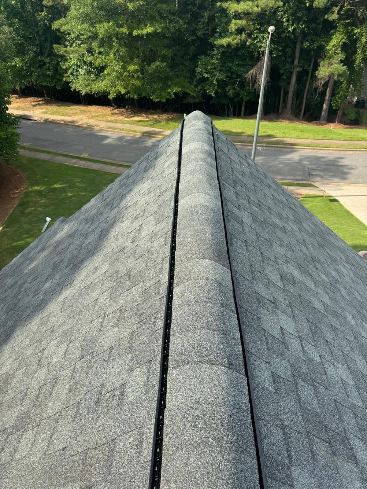Gray shingled roof ridge leading toward a tree-lined street below