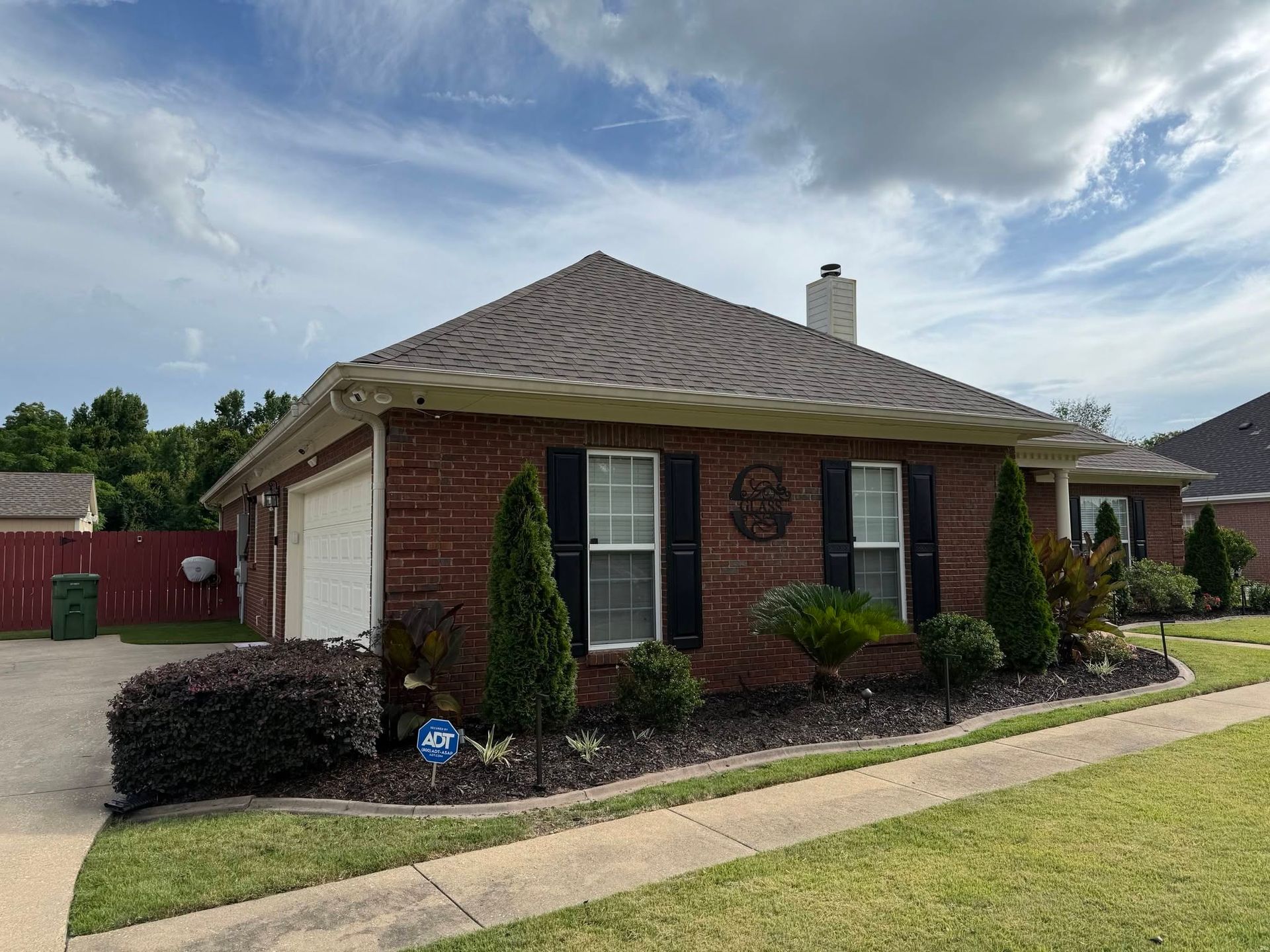 Brick house with a wavy roof, red shutters, and a manicured lawn under a cloudy sky