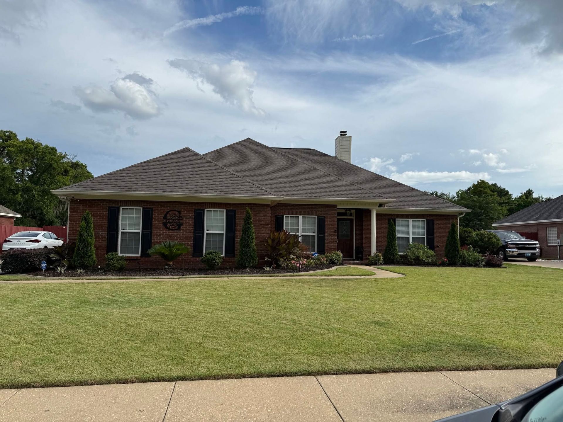 Single-story brick house with a brown roof, front lawn, and cloudy sky