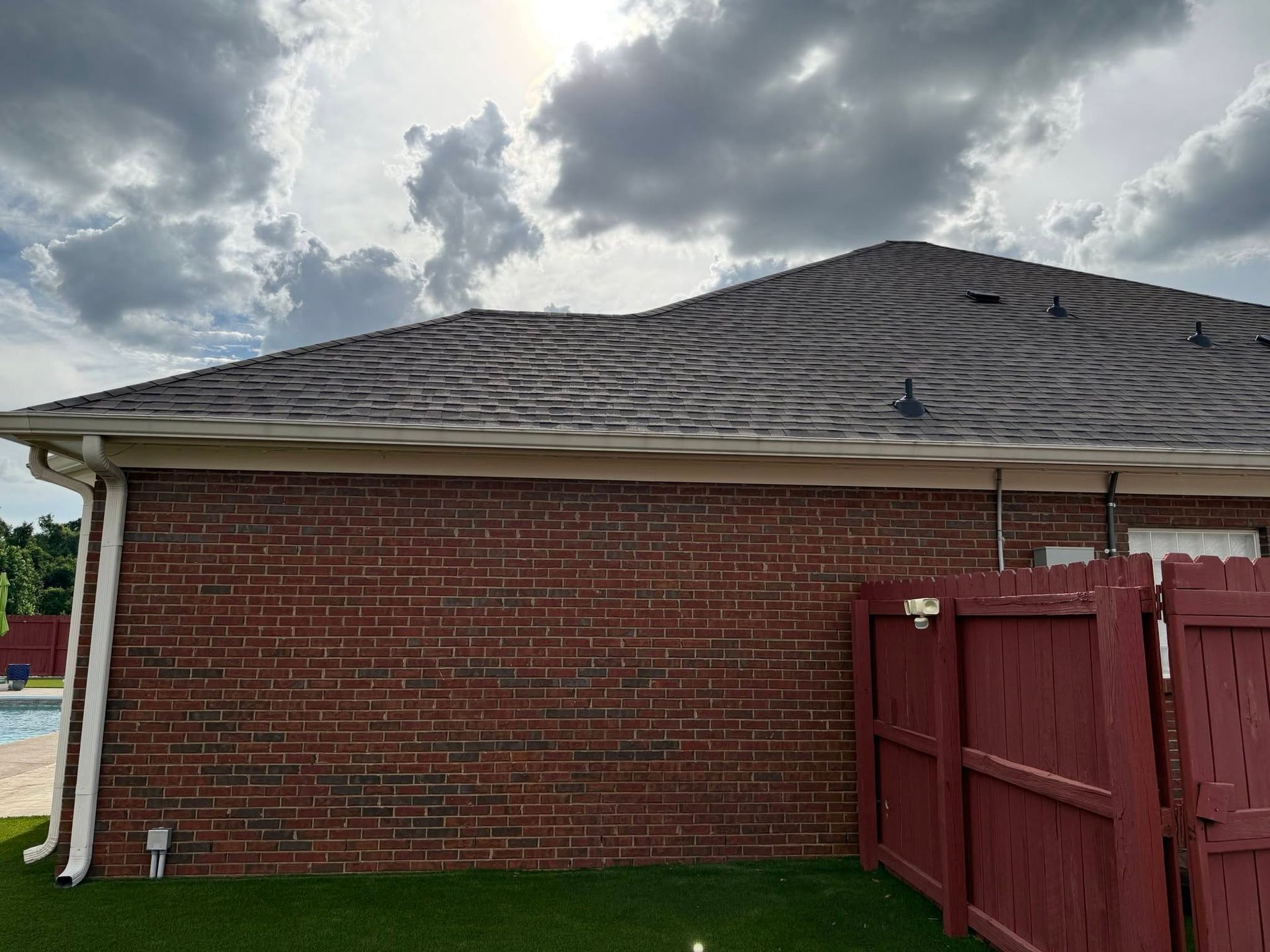 Brick building with dark shingle roof and red fence under cloudy sky
