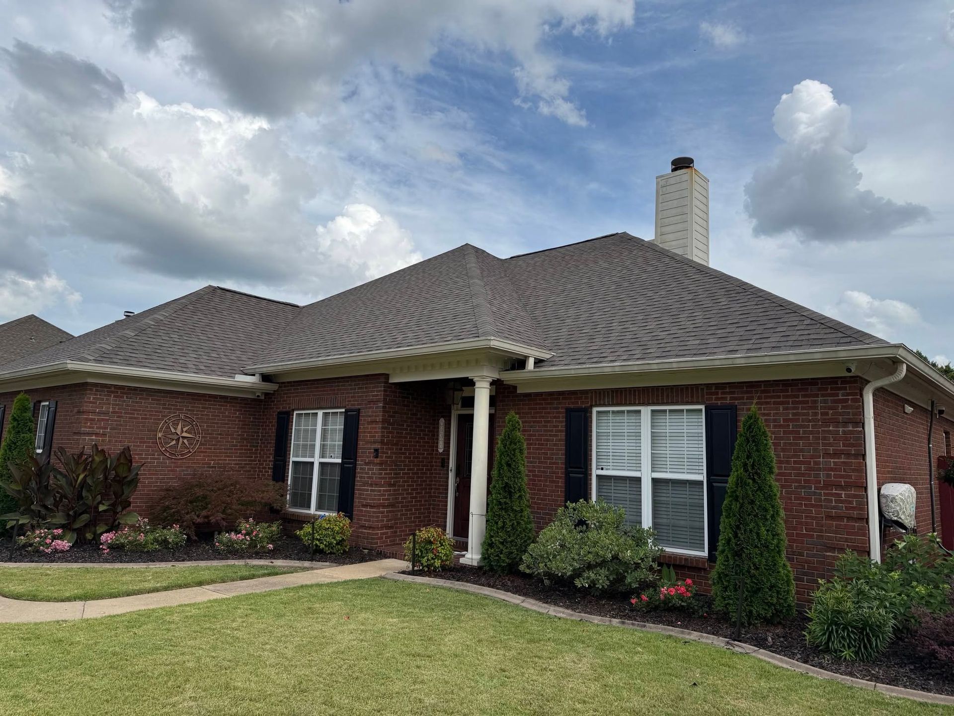 Brick ranch house with a gray shingled roof, white columns, and manicured lawn under cloudy sky