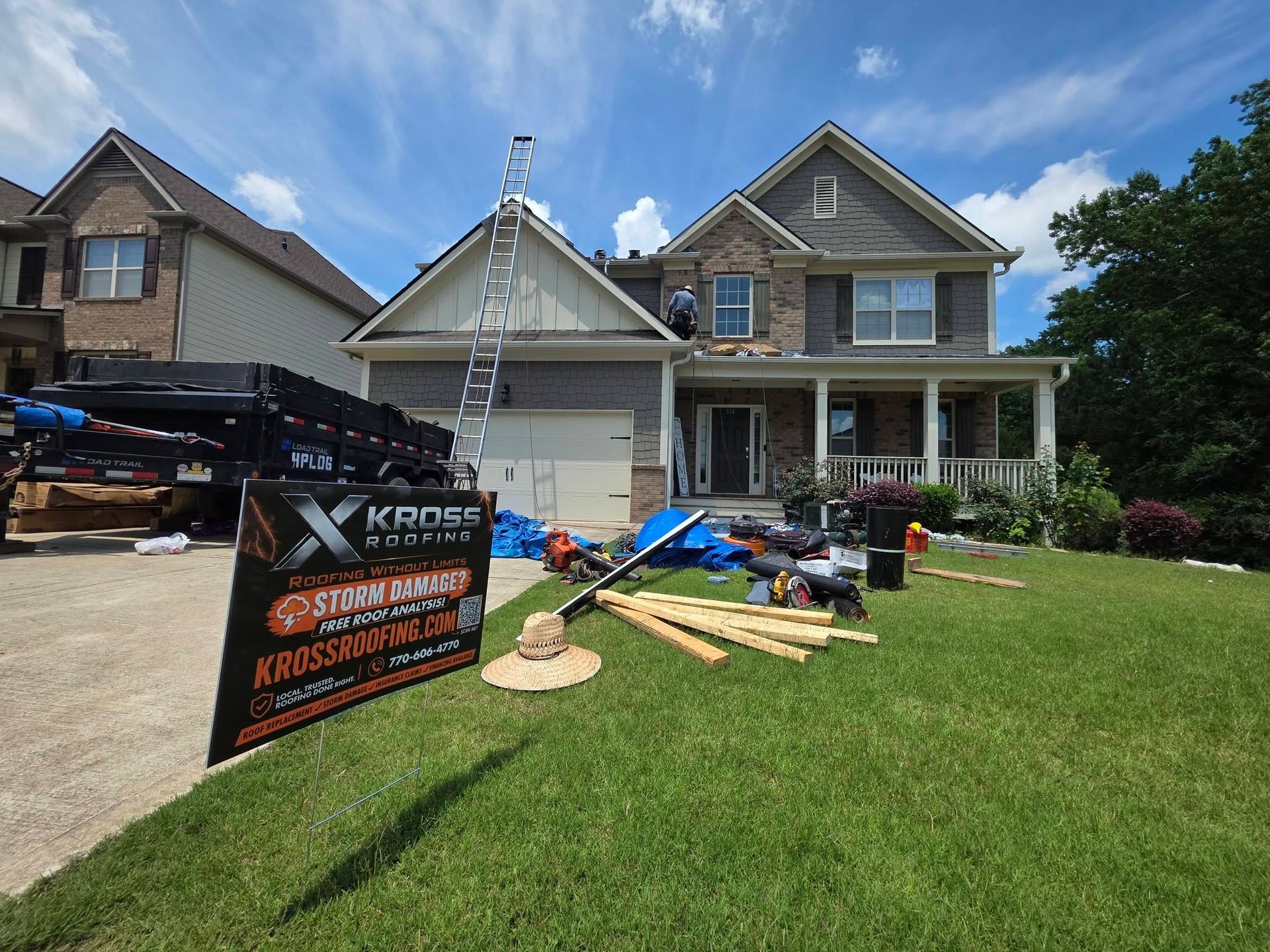 Two-story house with roof repair materials and a contractor sign on the front lawn