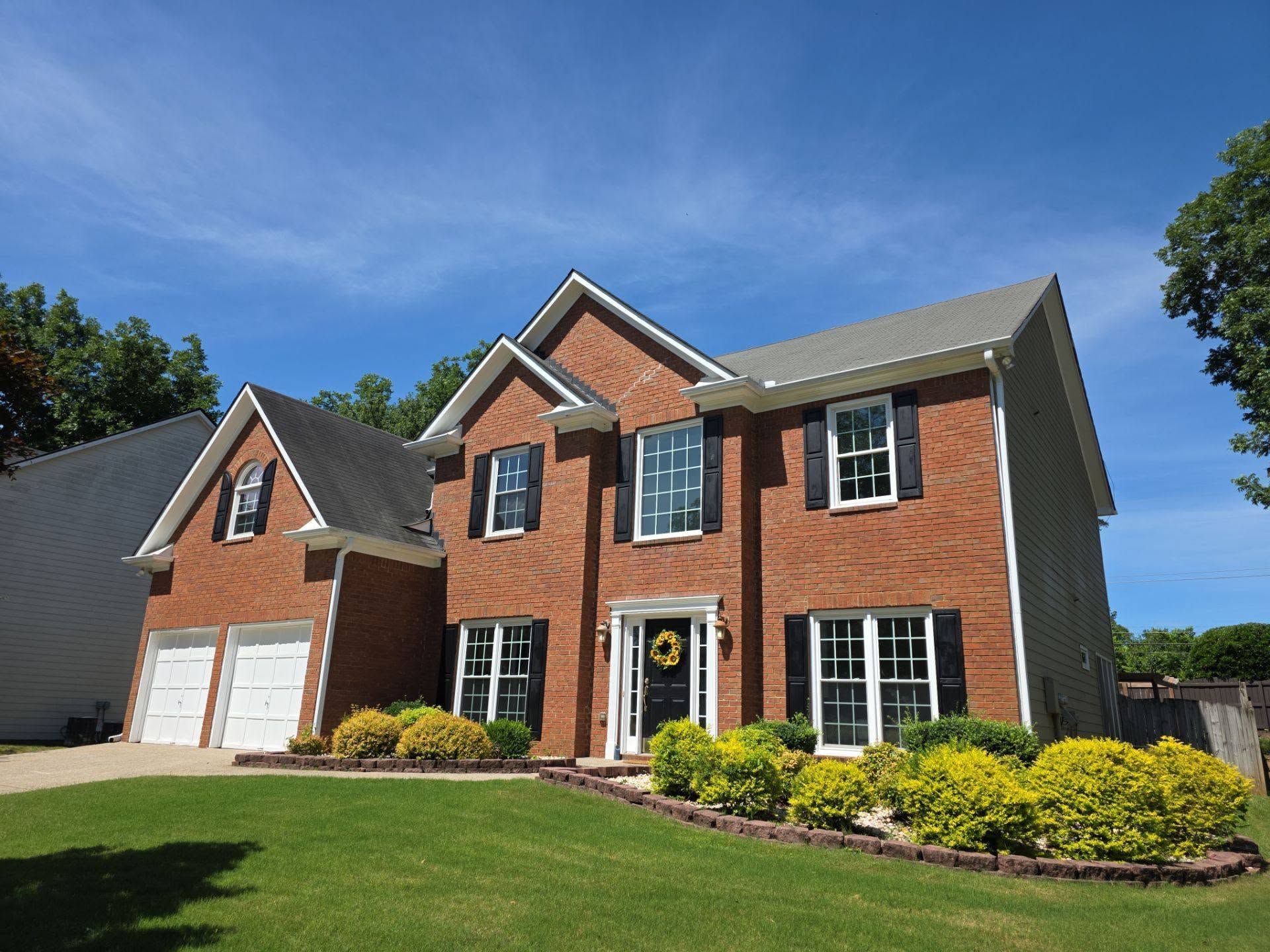 Two-story red brick suburban house with a double garage, front lawn, and blue sky