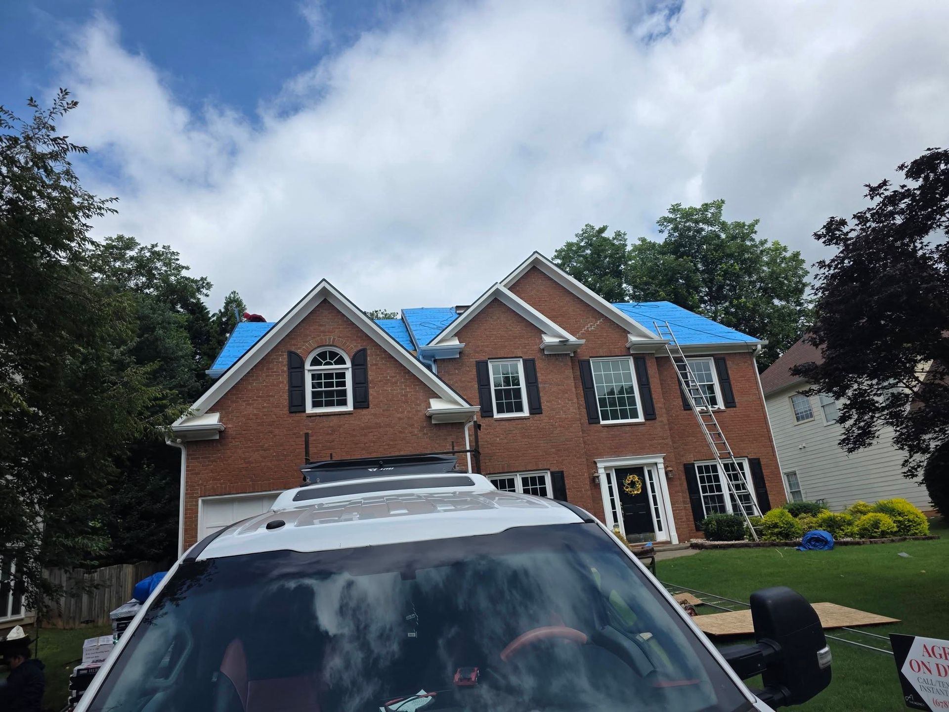 Brick suburban house with blue roof accents and a car in the driveway under a cloudy sky