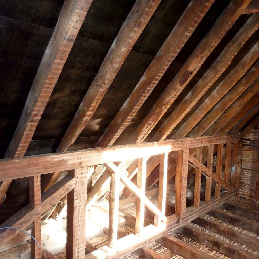 Wooden roof beams in a structure, with an interior view. Sunlight filters in.