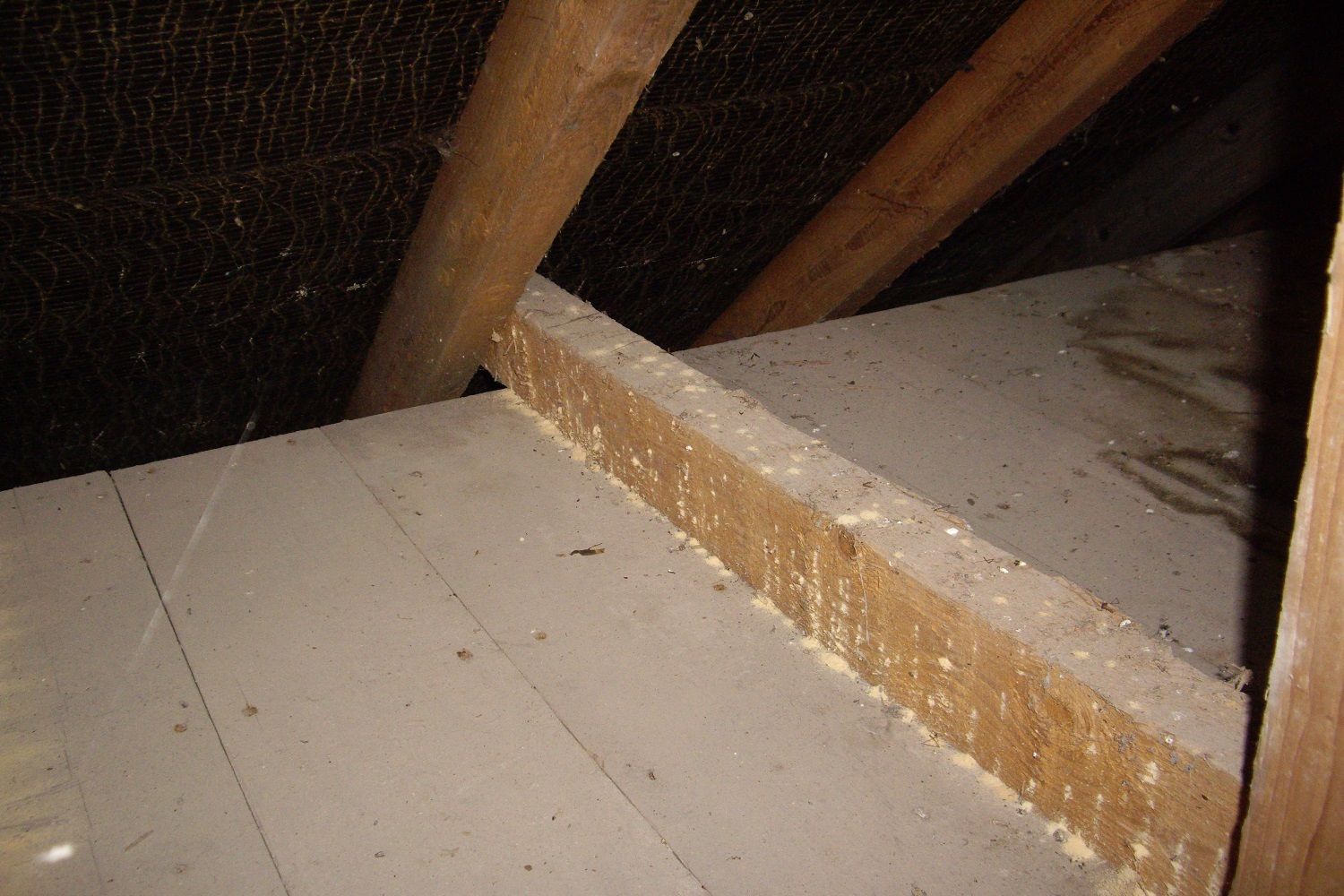 Attic interior showing wooden beams, insulation, and partially covered floorboards.